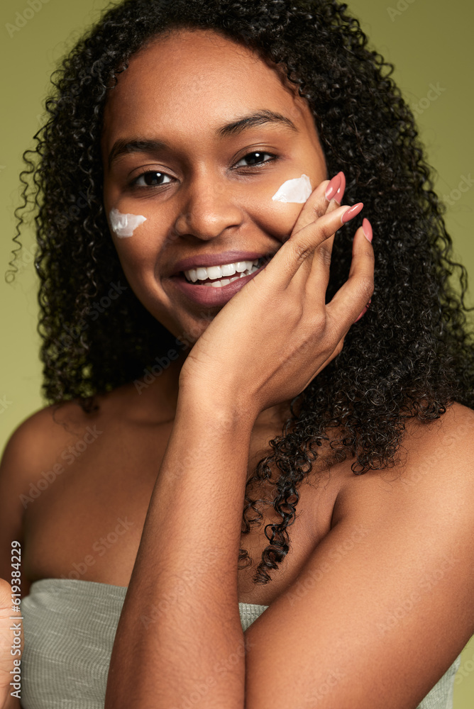 Smiling Hispanic woman applying cream on cheeks Smiling Hispanic woman applying cream on cheeks