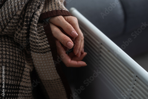 Woman warming hands near heater indoors, closeup