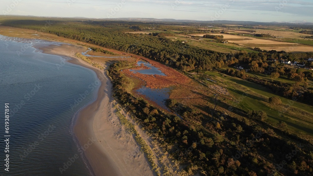 Aerial view of a body of water surrounded by greenery and a beach on a sunny day