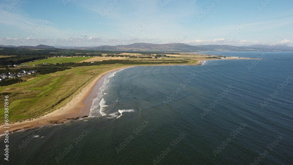 Aerial view of a body of water surrounded by greenery and a beach on a sunny day