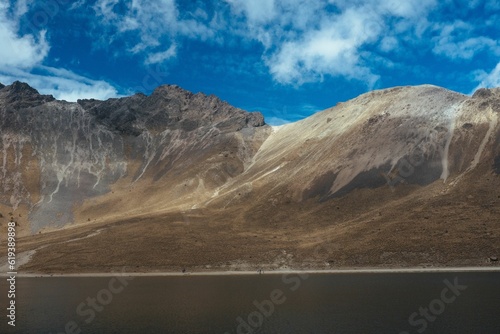 Scenic shot of a dry mountainous landscape surrounding a lake with a bright blue sky in the back
