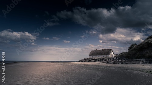 Scenic view of a house on a sandy beach under a cloudy blue sky