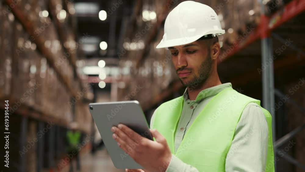 Professional Male Worker Wearing Hard Hat Utilizes Digital Tablet to Manage Stock in Retail Storage Filled with Shelves of Goods. People Working in Distribution Center Professional Male Worker Wearing Hard Hat Utilizes Digital Tablet to Manage Stock in Retail Storage Filled with Shelves of Goods. People Working in Distribution Center