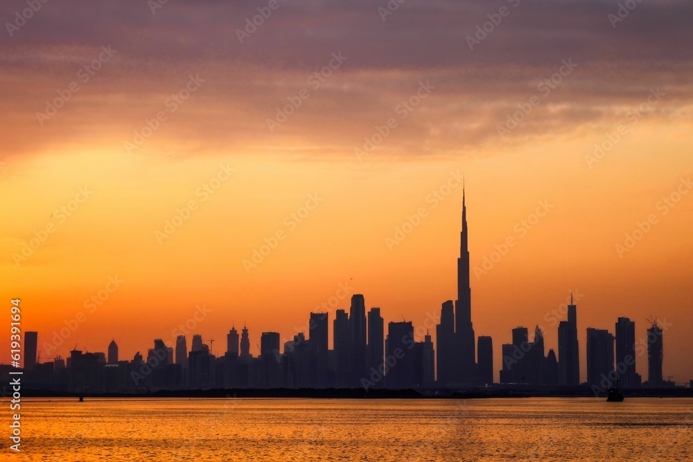 Silhouette view of Dubai city skyline against the orange dusk sky as seen from the sea at sunset