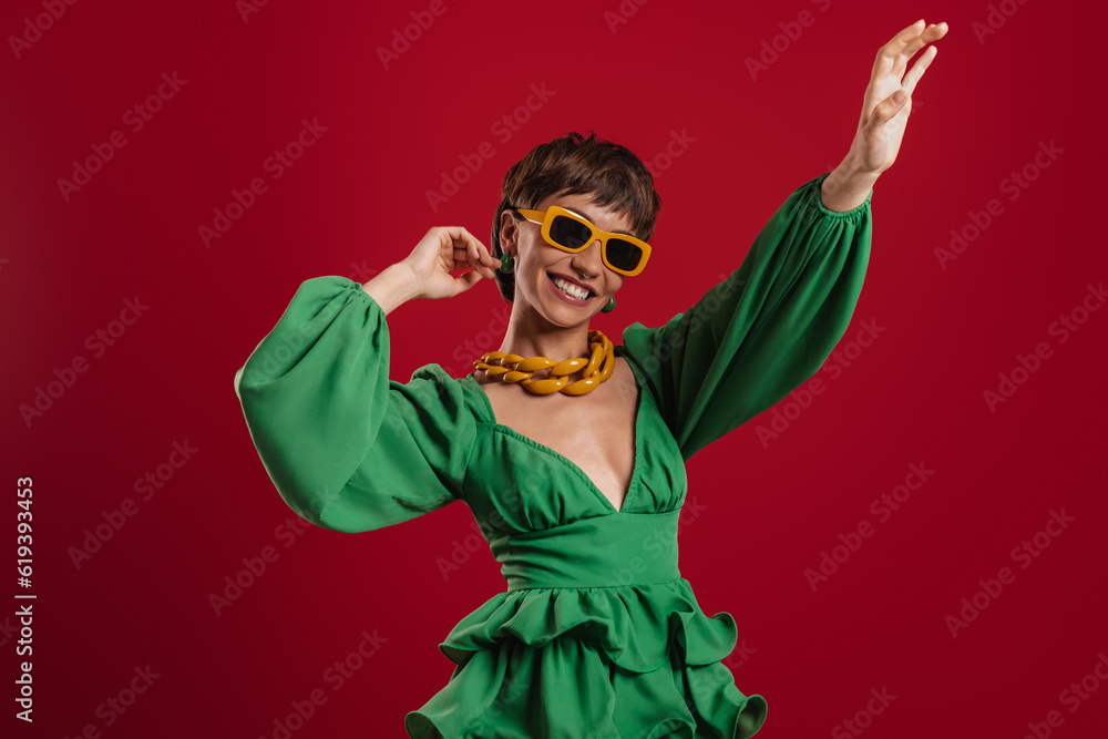 Joyful young short hair woman in elegant dress dancing against red background