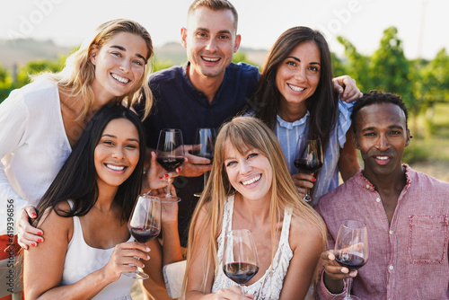 Group of young multiracial people smiling on camera while tasting wine at wineyard during summer time - Diverse friendship concept