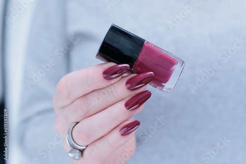 Woman hand with long nails and a bottle of dark red burgundy nail polish photo