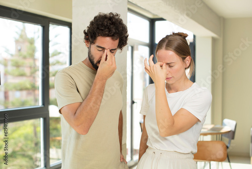 young adult couple feeling stressed, unhappy and frustrated, touching forehead and suffering migraine of severe headache