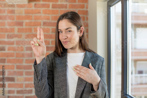 young adult pretty woman looking happy, confident and trustworthy, smiling and showing victory sign, with a positive attitude