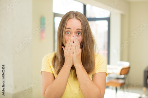 pretty blond woman looking happy  cheerful  lucky and surprised covering mouth with both hands