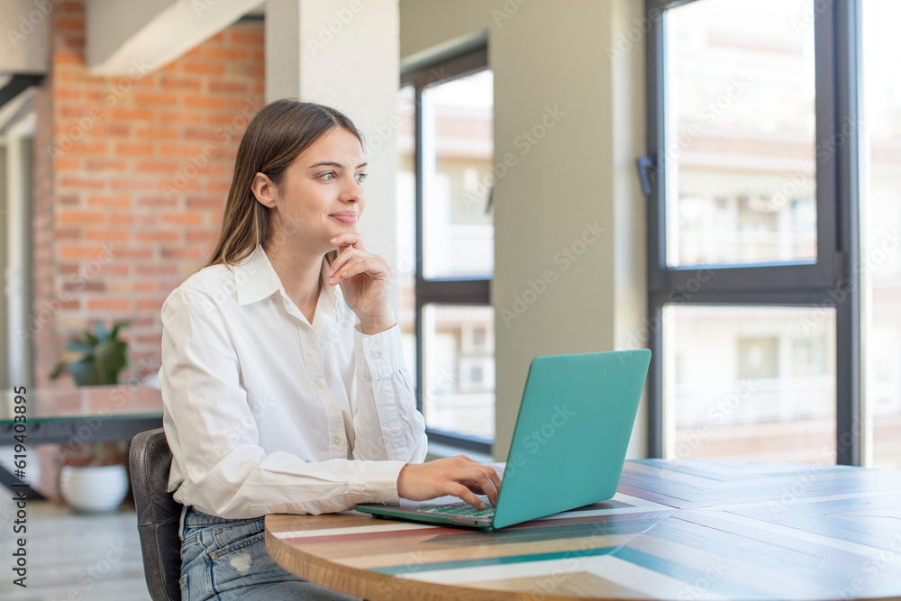 young pretty woman smiling with a happy, confident expression with hand on chin. working with a laptop young pretty woman smiling with a happy, confident expression with hand on chin. working with a laptop
