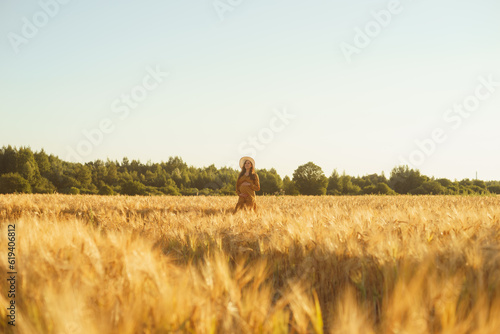 Pregnant woman in the rays of the sunset. Beautiful young girl is walking in the field expecting the birth of a child. Motherhood, pregnancy and happiness concept.