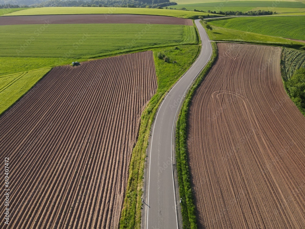 Long asphalt road between agriculture land with soil and wheat from above 
