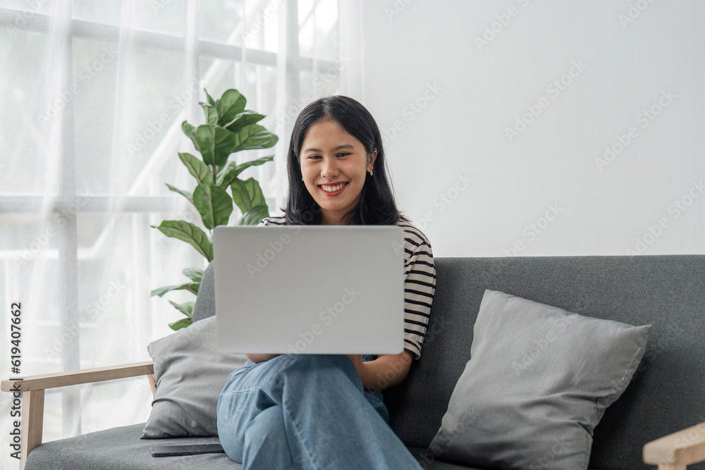 Thoughtful young woman using computer while sitting on the sofa surfing the net at home