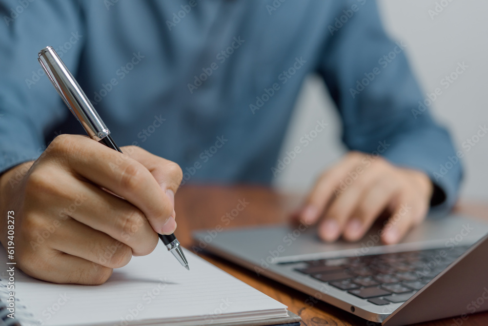 Man Writing with Pen on Notebook and laptop on desk. Business Success, and Effective Planning management and productivity in office environment. Man Writing with Pen on Notebook and laptop on desk. Business Success, and Effective Planning management and productivity in office environment.