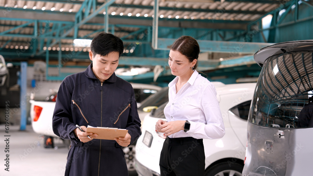 Obraz premium Professional mechanic in a suit working in a garage The mechanic talks to the customer and agrees to fix the car successfully. Send contract to pick up the car. The two shook hands with satisfaction.