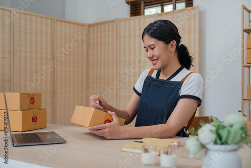 Woman runs an ecommerce business is writing a list of customers on box before shipping to customer, Concept of selling products online