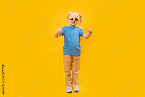 Full-leight portrait of girl in blue T-shirt and sunglasses showing thumbs up. Copy space, mock up