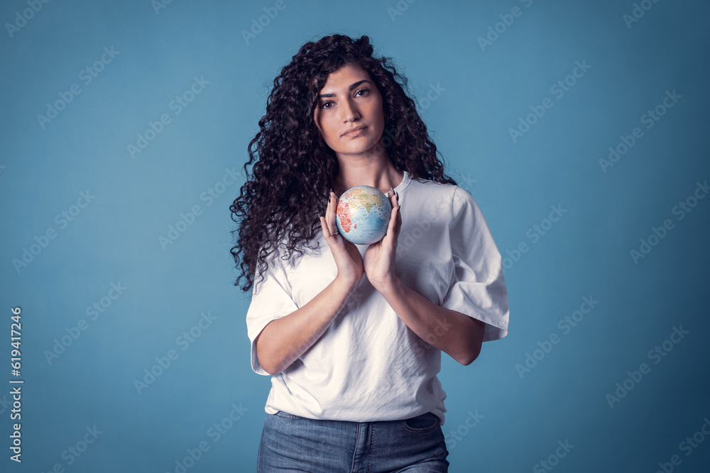 Studio shot of beautiful confident caucasian curly model woman wears blue jeans and casual basic solid white t-shirt, isolated over blue background. Pretty brunette holding small planet in her hands Studio shot of beautiful confident caucasian curly model woman wears blue jeans and casual basic solid white t-shirt, isolated over blue background. Pretty brunette holding small planet in her hands
