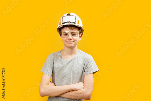 Caucasian teenager boy wears glasses and helmet crossed his arms across his chest and looks into the camera on yellow background. Copy space. photo