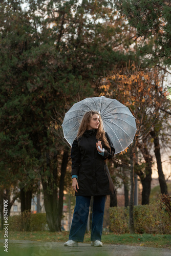 Beautiful smiling young woman under transparent umbrella in autumn park. Girl in black coat walks on the rain © somemeans