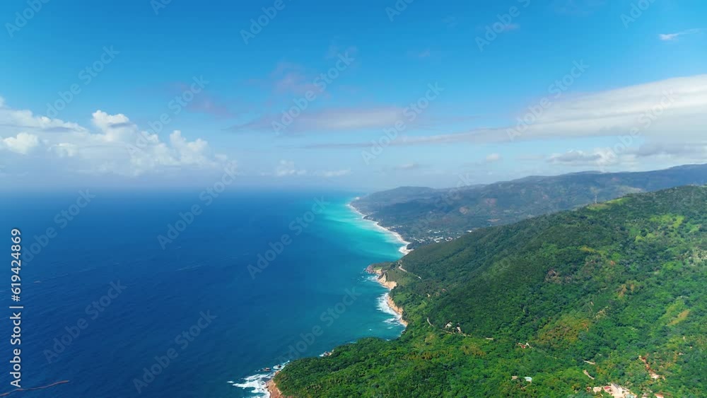 Bird's-eye view of the Caribbean coastline with green hills against the blue ocean. Dominican wildlife landscape on a sunny summer day. Aerial view of high mountains and blue sea. Bird's-eye view of the Caribbean coastline with green hills against the blue ocean. Dominican wildlife landscape on a sunny summer day. Aerial view of high mountains and blue sea.