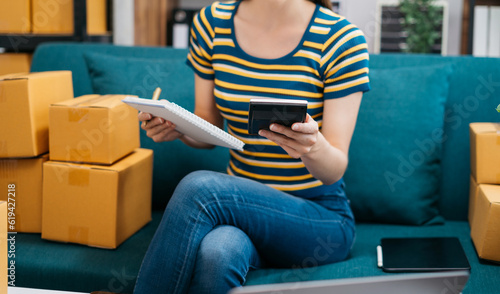 Entrepreneur using calculator with pencil in her hand, calculating financial expense at home office, online market packing box delivery,Startup successful small business owner, SME, concept.