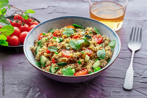 Quinoa tabbouleh salad in a bowl, a healthy dinner with tomatoes and mint on a purple background