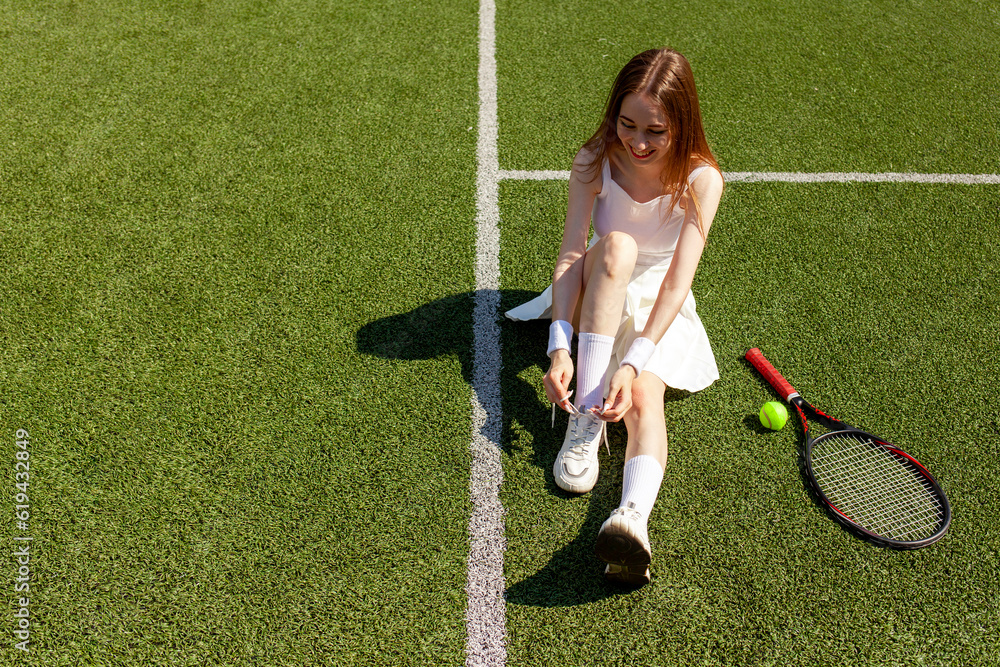 young girl tennis player in white sports uniform ties her