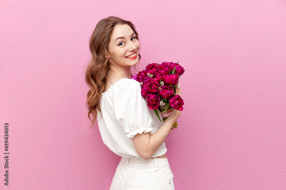 young attractive girl in white clothes holds bouquet of pink tulips and smiles, woman on holiday with flowers young attractive girl in white clothes holds bouquet of pink tulips and smiles, woman on holiday with flowers
