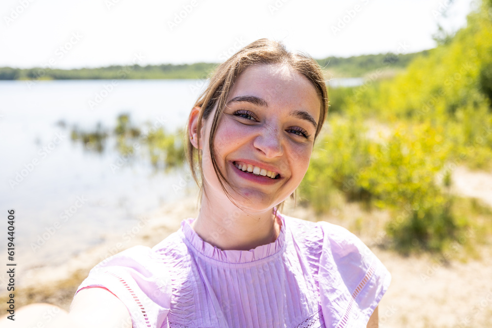 Capture the essence of summer adventure as an attractive young brunette immerses herself in nature's beauty, making a selfie with her smartphone by the tranquil forest lake. This captivating moment Capture the essence of summer adventure as an attractive young brunette immerses herself in nature's beauty, making a selfie with her smartphone by the tranquil forest lake. This captivating moment