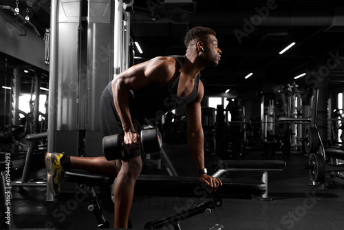 athletic african american man trains in dark gym  athletic guy lifts heavy dumbbells in fitness club