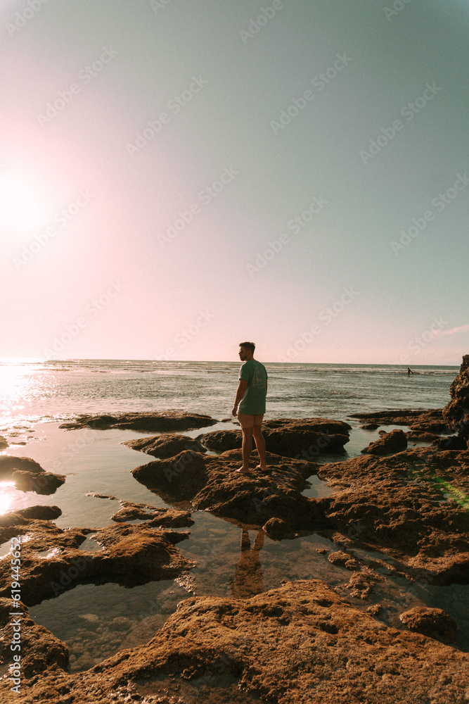 Podróżnik o zachodzie słońca na tle oceanu stojący przy skałach. - obrazy, fototapety, plakaty 