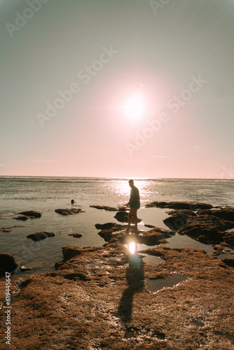 Podróżnik o zachodzie słońca na tle oceanu stojący przy skałach.