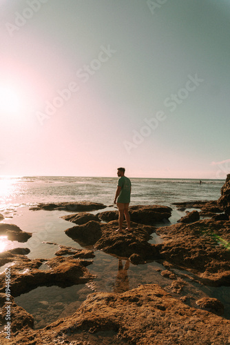 Podróżnik o zachodzie słońca na tle oceanu stojący przy skałach.