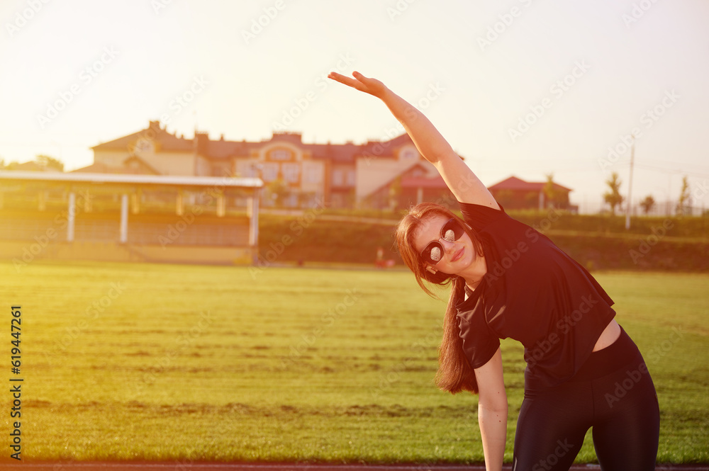Young attractive girl in sports tight clothes doing stretching exercises and warming up for jogging in the stadium early in the morning. Woman runner stretching muscles. The concept of health life