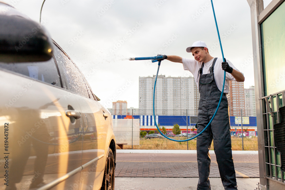 young guy in uniform car wash worker covers the car with foam from hose young guy in uniform car wash worker covers the car with foam from hose