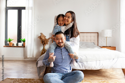happy asian family sit together at home in the bedroom and smile, little korean girl sits on the shoulders of her dad © Богдан Маліцький