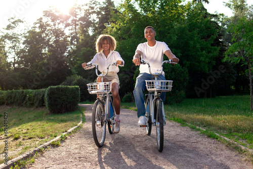 african-american couple rides bicycles in the park and talks, man and woman walk on eco-transport
