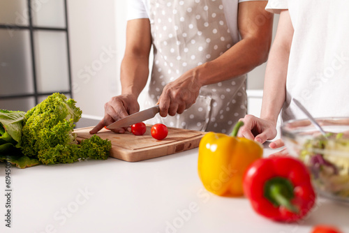 african american man in an apron cuts tomatoes in the kitchen, close-up, multiracial couple prepares