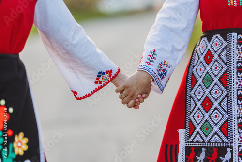 Girls in traditional bulgarian ethnic costumes with folklore embroidery holding hands. The spirit of Bulgaria - culture, history and traditions.