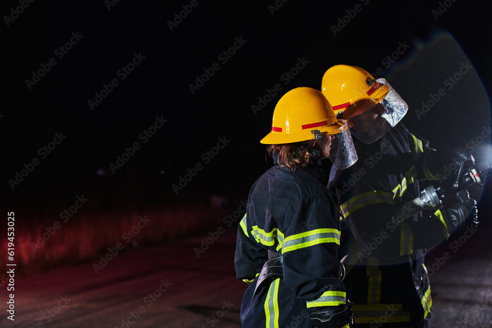 Firefighters using a water hose to eliminate a fire hazard. Team of female and male firemen in dangerous rescue mission. Firefighters using a water hose to eliminate a fire hazard. Team of female and male firemen in dangerous rescue mission.