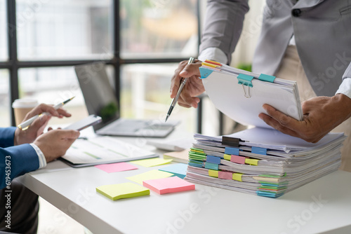 Businessman man working in stacks of papers searching for unfinished paperwork information on form check stack on table and checking financial papers in busy workload photo