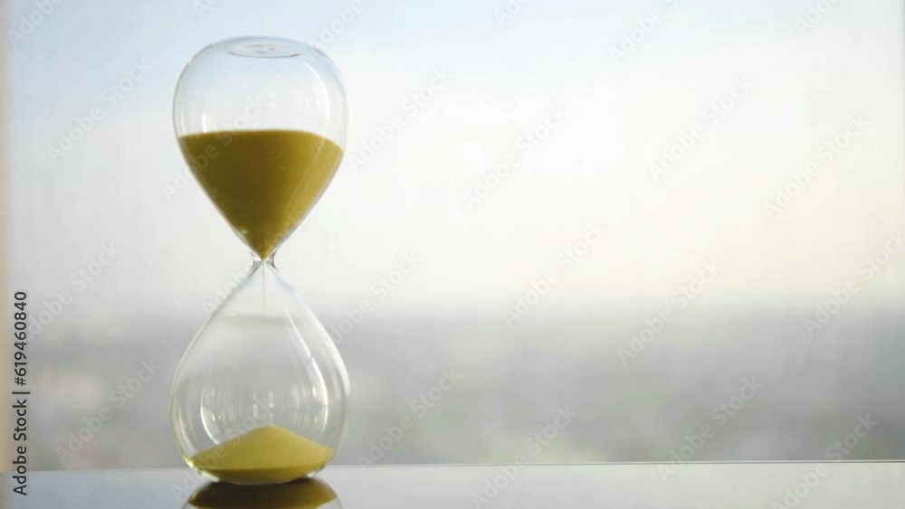 hourglass on table, sand flowing through the bulb of sandglass, time is money concept, times passing concept like work or business deadline, resemble urgency running out of occasion in life