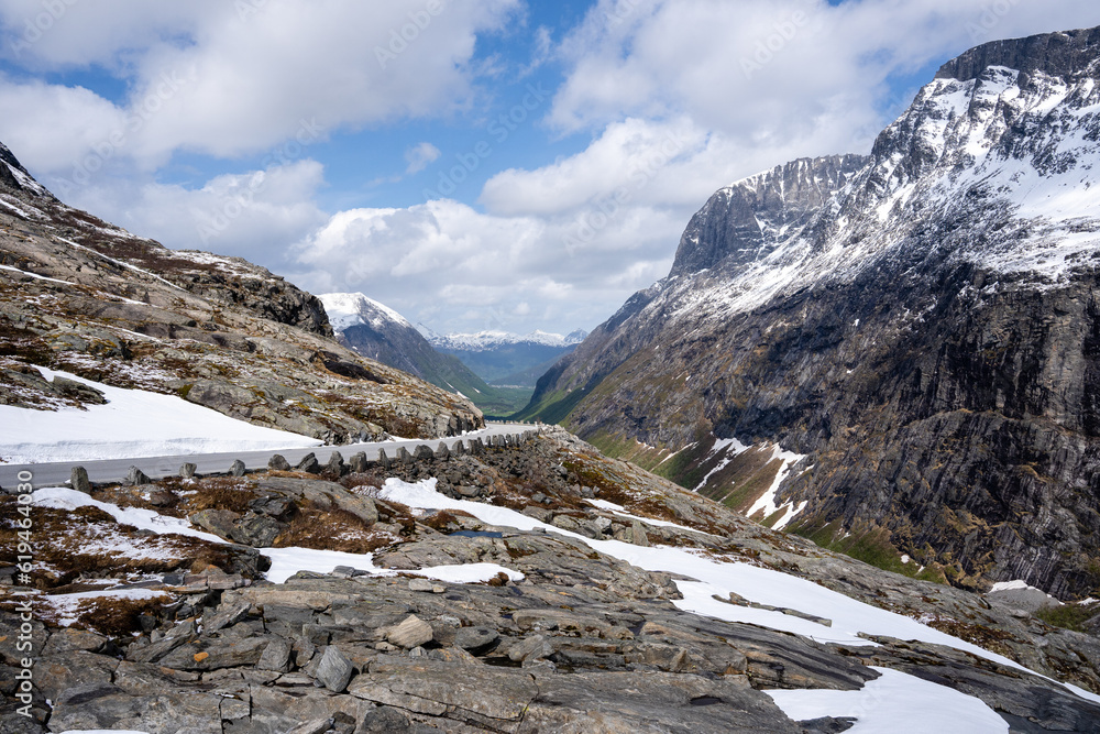 mountain and the rocks are gray but above them is a blue sky with white clouds and green grass can be seen at the bottom of the mountain