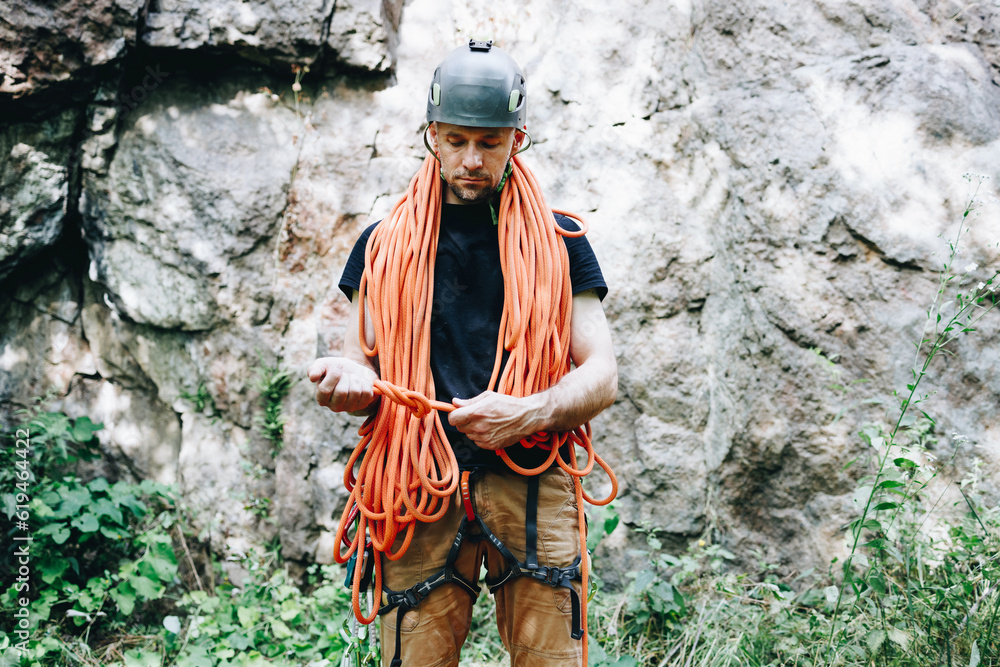 Male rock climber with climbing equipment holding rope ready to start climbing the route