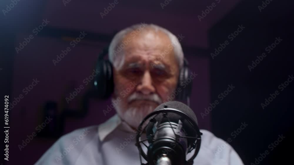 The old man creates a podcast in a professional studio. Senior male does online streaming interviews. Elderly man blogger speaking in microphone or make vlog. Recording audio content for social media The old man creates a podcast in a professional studio. Senior male does online streaming interviews. Elderly man blogger speaking in microphone or make vlog. Recording audio content for social media