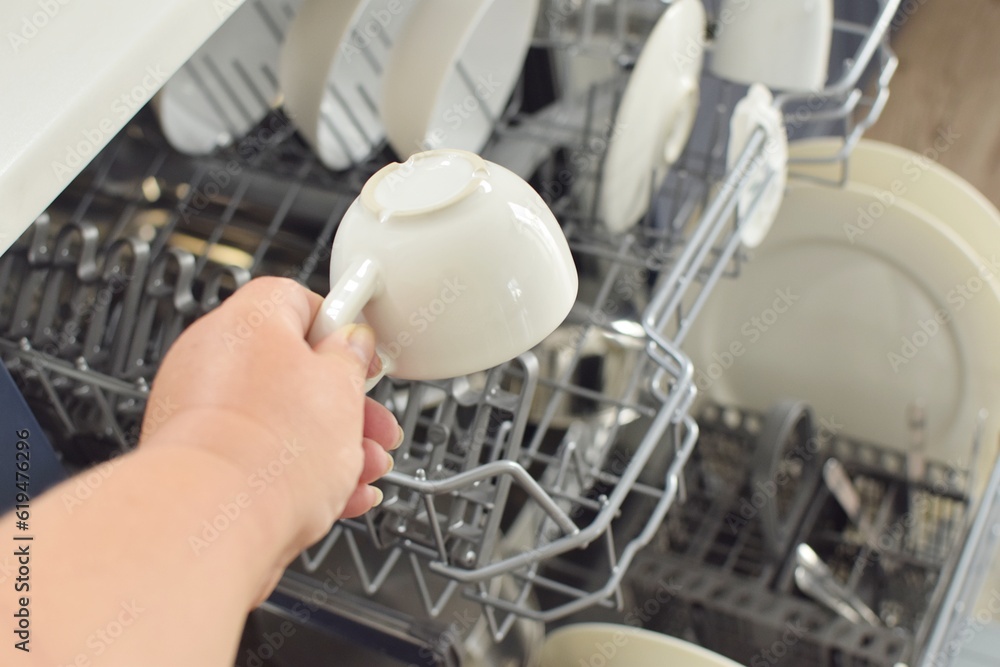 woman puts a white mug in the dishwasher woman puts a white mug in the dishwasher