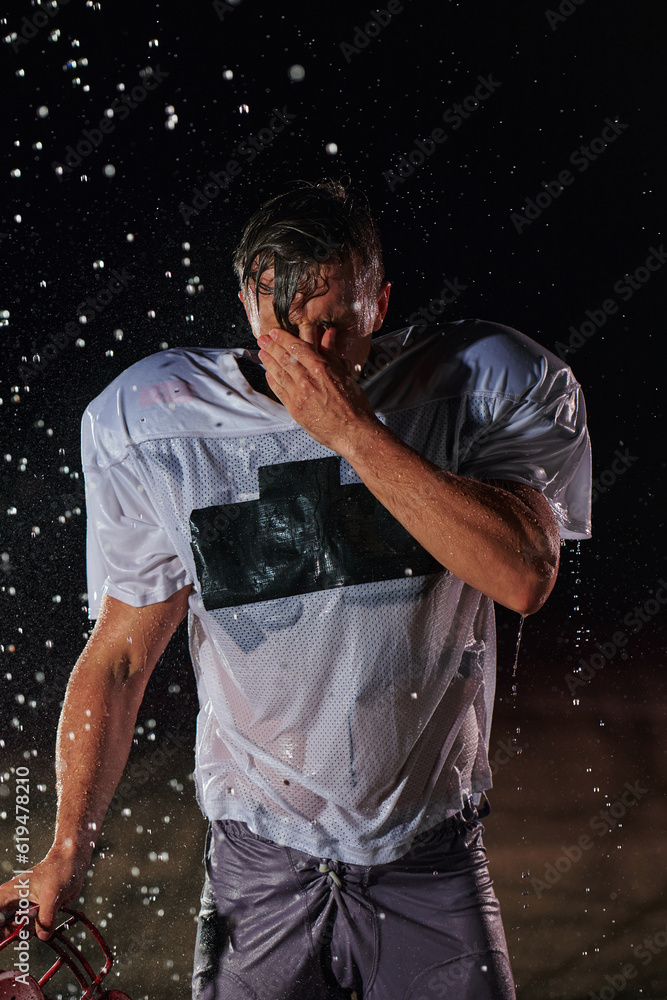 American Football Field: Lonely Athlete Warrior Standing on a Field Holds his Helmet and Ready to Play. Player Preparing to Run, Attack and Score Touchdown. Rainy Night with Dramatic Fog, Blue Light