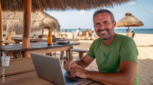 40 years old man at the beach cocktail bar, working on the laptop at distance from office , teleworking concept